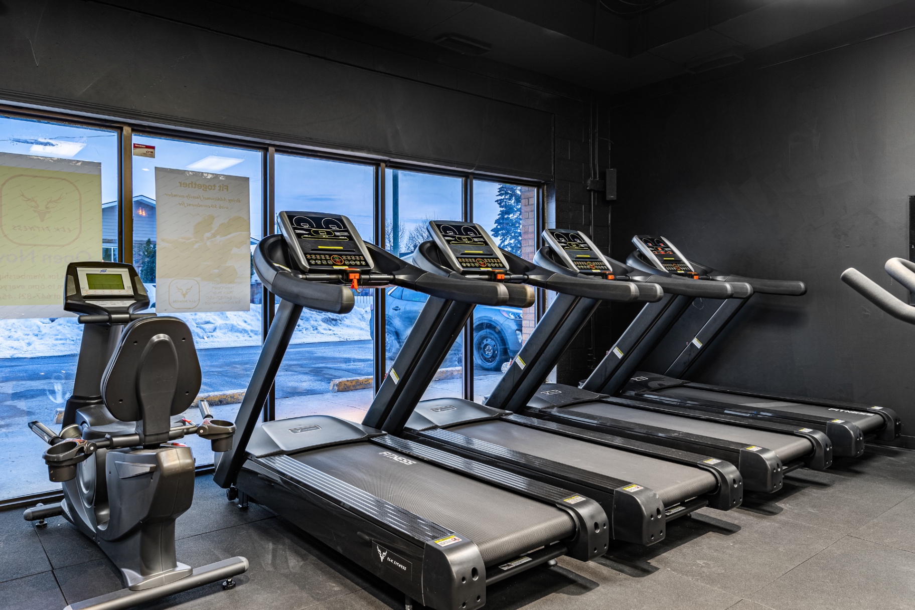 Treadmills lined along Elk Fitness Didsbury storefront windows at dusk