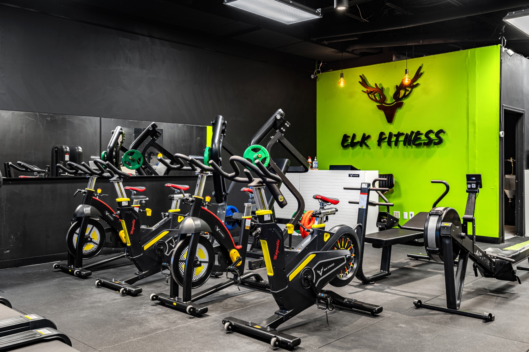 Spin bikes and rower in front of the Elk Fitness logo wall